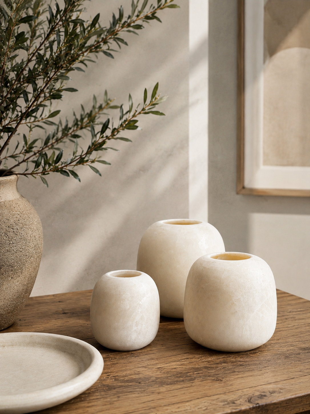 Three smooth, rounded, off-white stone vessels of varying heights arranged together. Each vessel features a small, circular opening at the top and a polished, solid surface with subtle natural veining throughout the material.