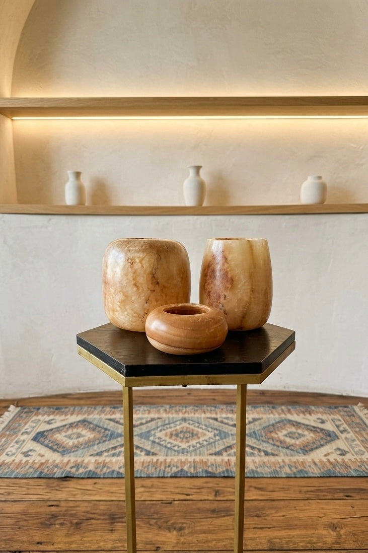 Three smooth, rounded, off-white stone vessels of varying heights arranged together. Each vessel features a small, circular opening at the top and a polished, solid surface with subtle natural veining throughout the material.